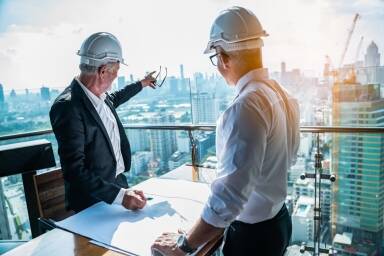 2 hommes avec casque de sécurité devant plan de construction et regardant au loin l'avancée d'un chantier